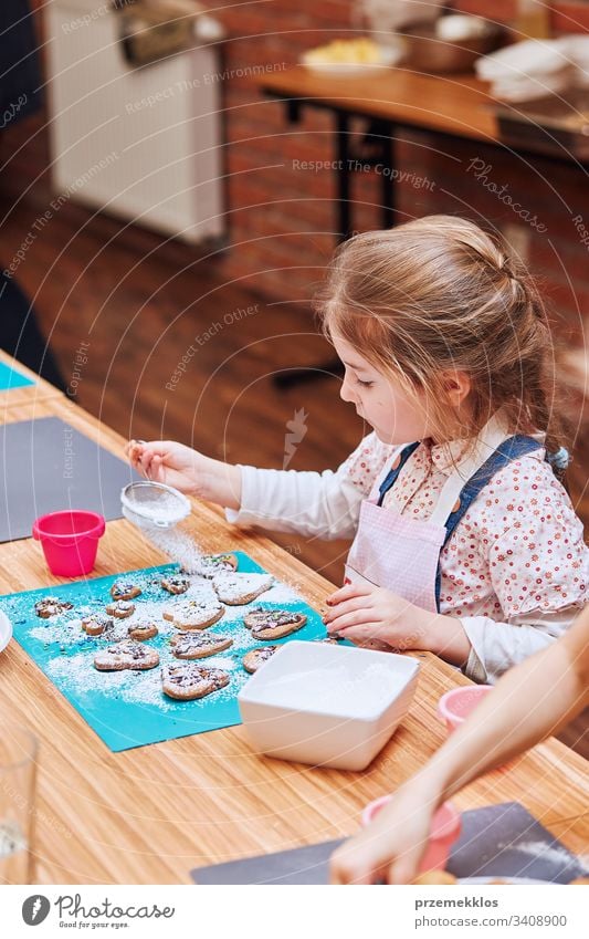 Little girl decorating her baked cookies with colorful sprinkle and icing sugar. Kid taking part in baking workshop. Baking classes for children, aspiring little chefs. Learning to cook. Combining and stirring prepared ingredients