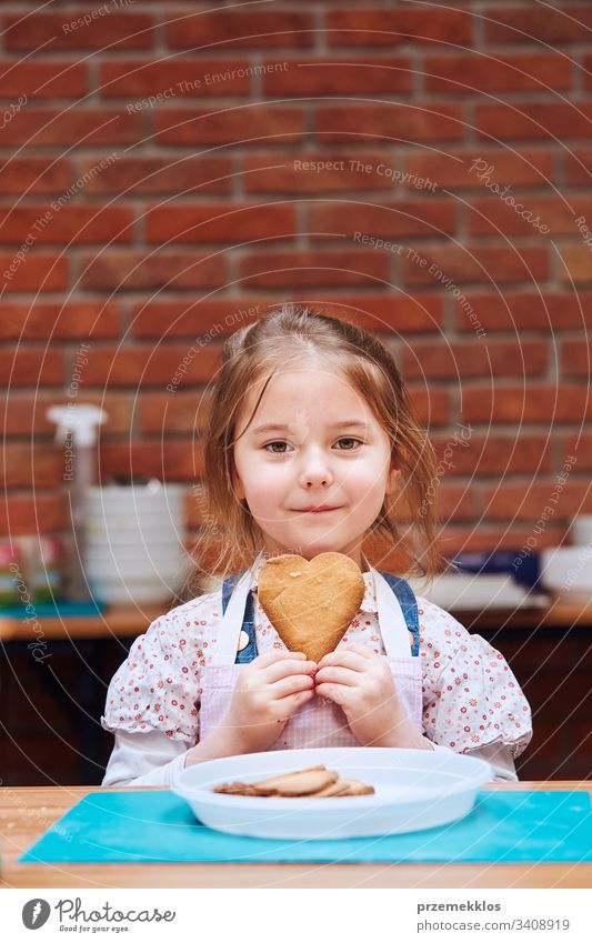 Little girl getting happy out of baked cookie made oneself. Kid taking part in baking workshop. Baking classes for children, aspiring little chefs. Learning to cook. Combining and stirring prepared ingredients. Real people, authentic situations