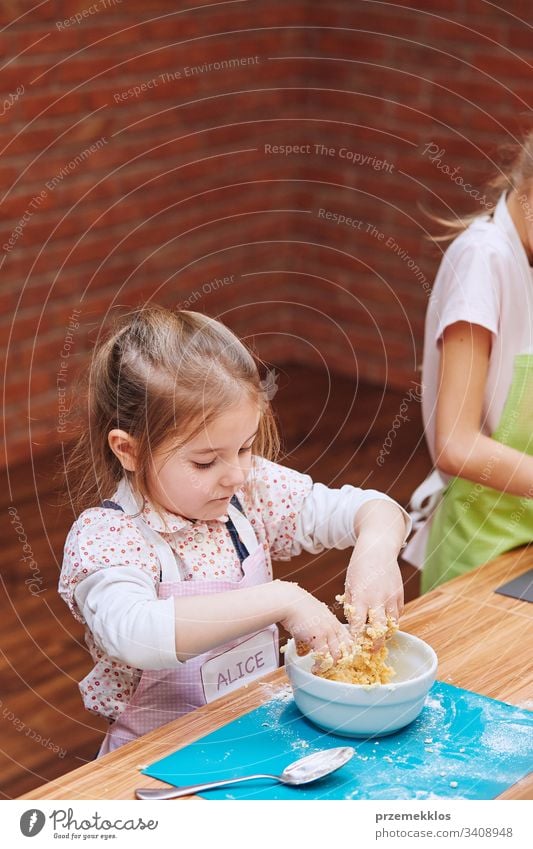 Little girls kneading the dough for baking the cake. Kids taking part in baking workshop. Baking classes for children,  aspiring little chefs. Learning to cook. Combining and stirring prepared ingredients. Real people, authentic situations
