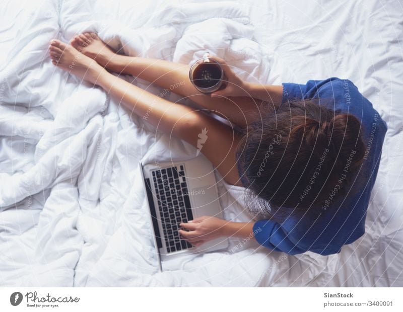Young woman drinking coffee at home in her bed and checking her laptop cozy morning cup girl book legs soft view young warm bedroom beautiful white hands