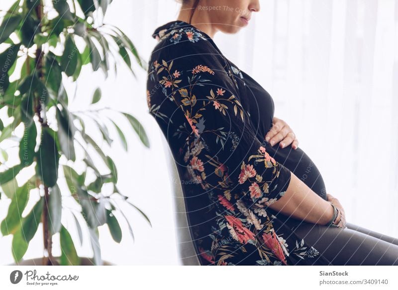 Pretty young pregnant woman sitting by the window pregnancy beautiful belly happy life home maternity care baby concept plants expectation abdomen female mother