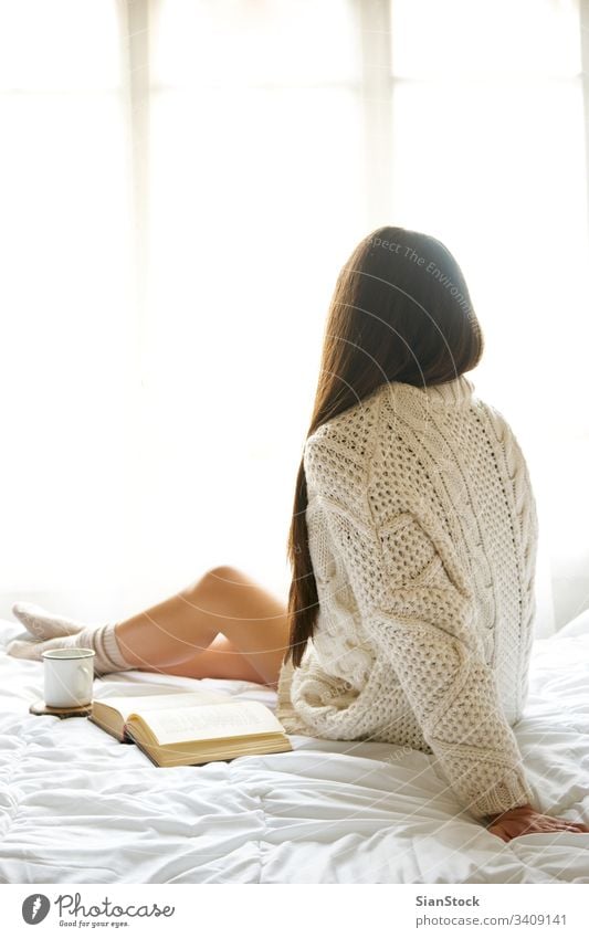 Soft photo of woman on the bed with old book and cup of coffee read reading window view lazy sunday winter tea morning girl home relax socks beautiful young