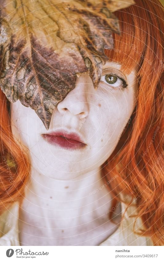 Redhead young woman covering by a dry autumn leaf fall leave portrait art artistic redhead red hair delicate face ginger concept conceptual youth orange yellow