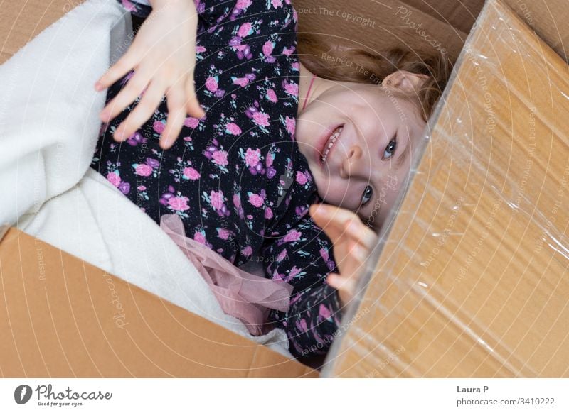 Little blonde girl hiding in a cardboard box peek a boo hide and seek family fun happiness happy enjoy laughing small interior floor playful unpacking surprise