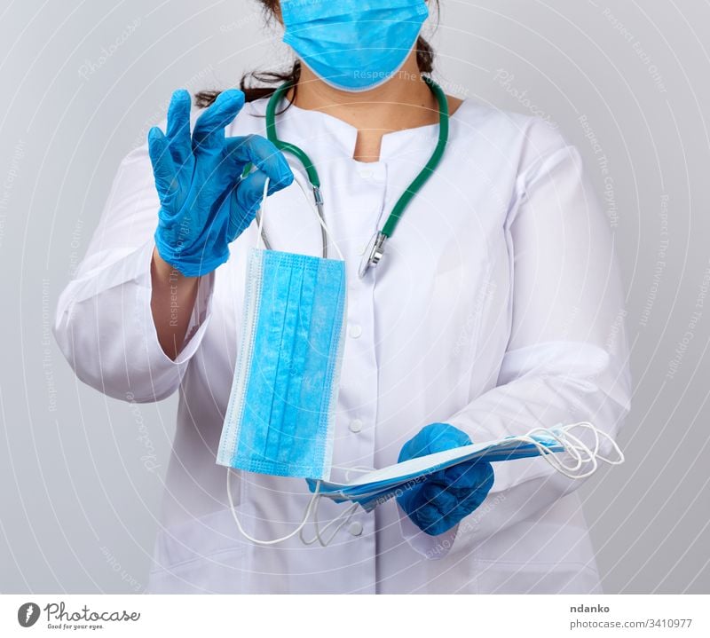 female doctor in a white coat and mask holds a stack of protective face masks about the virus adult assistant blue care caucasian clinic clinical equipment