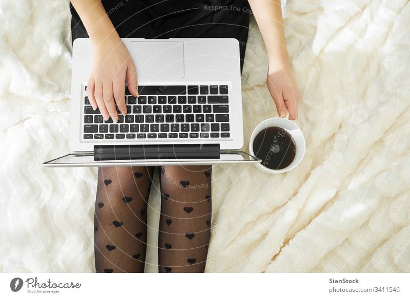 Young woman drinking coffee at home in her bed and checking her laptop computer cup young girl using white beautiful technology morning business socks person