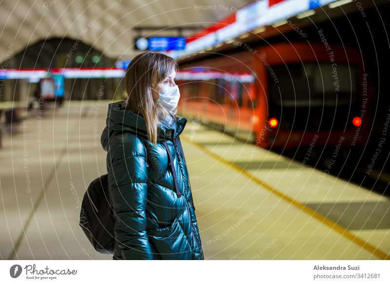 Woman in winter coat with protective mask on face standing on metro station, waiting for train, looking worried. Preventive measures in public places of epidemic regions. Finland, Espoo
