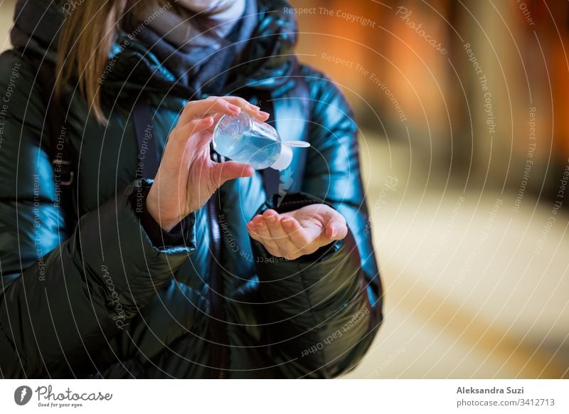 Woman in winter coat with protective mask on face standing on metro station, using hand sanitizer, looking worried. Preventive measures in public places of epidemic regions. Finland, Espoo