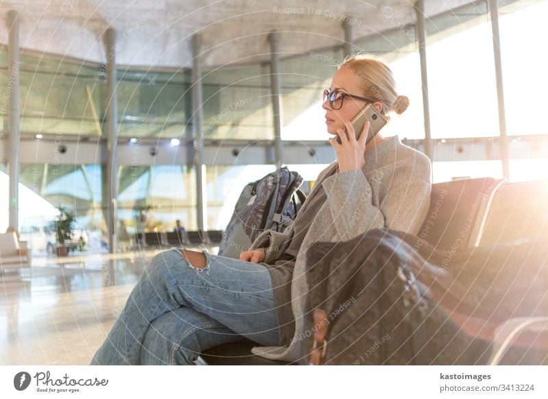 Female traveler talking on her cell phone while waiting to board a plane at departure gates at airport terminal. female woman business flight baggage luggage