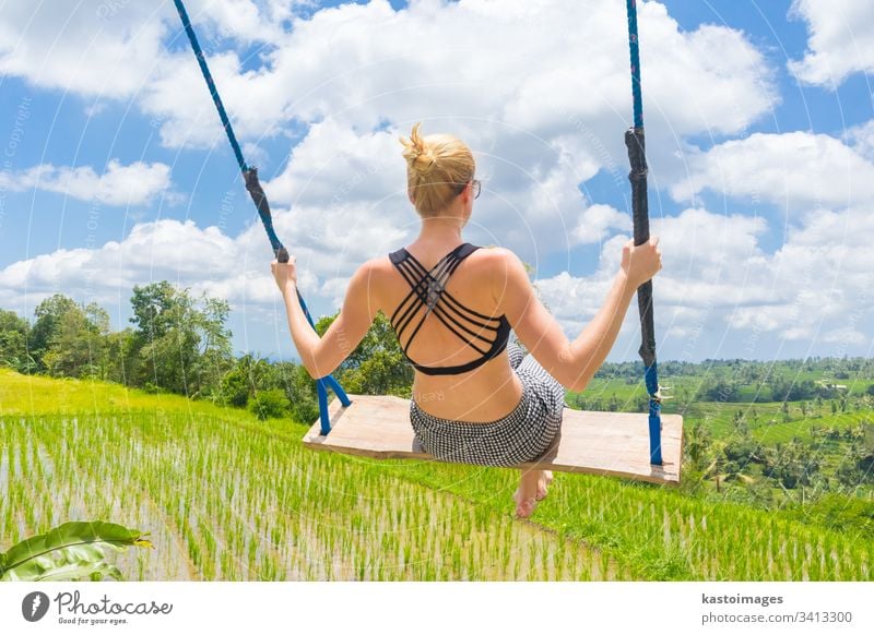 Happy female traveller swinging on wooden swing, enjoying summer vacation among pristine green rice terraces. woman free nature people person sky paradise girl
