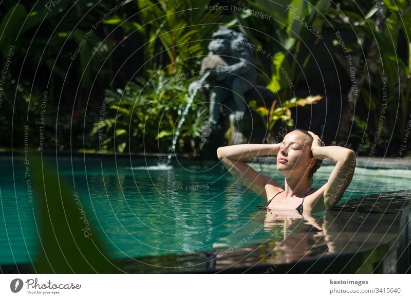 Sensual young woman relaxing in outdoor spa infinity swimming pool surrounded with lush tropical greenery of Ubud, Bali. wellness water nature beauty beautiful