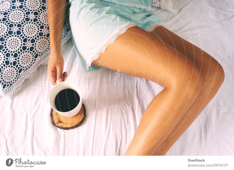 Young woman enjoying her coffee while sitting in bed. cozy morning cup girl home book legs soft socks top view young warm bedroom beautiful white hands comfort