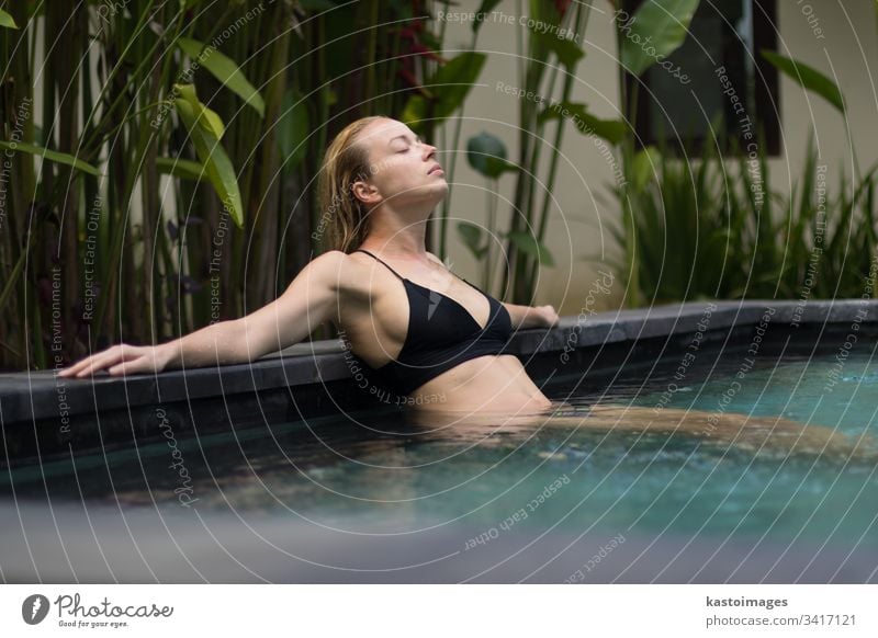 Sensual young woman relaxing in outdoor spa infinity swimming pool surrounded with lush tropical greenery of Ubud, Bali. wellness serenity sensual relaxation
