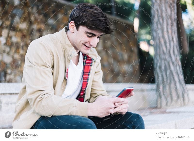 Young hispanic man using mobile phone while sitting outdoors male young 1 holding people photogenic modern guy person text portrait adult casual attire