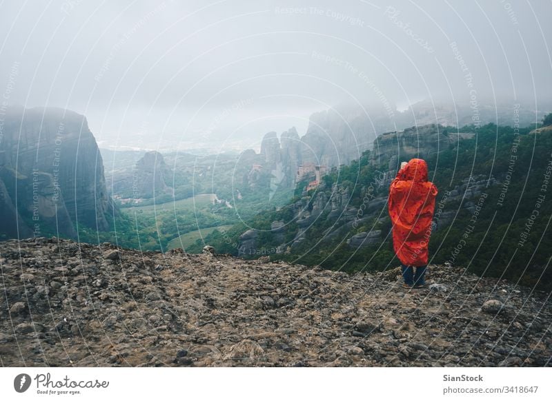 Woman with red raincoat takes photos with her smart phone on landscape of Meteora rocks, Greece meteora greece monastery fog mountain hiking tour hike girl