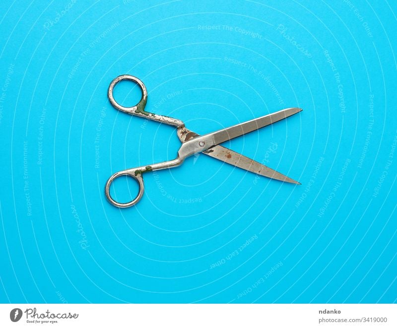 very old vintage metal tailor scissors on a blue background rusty sewing sharp open antique big blade clipping closeup craft cut design domestic equipment hand