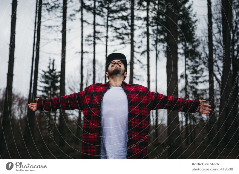 Excited guy enjoying fresh air of beautiful woods man forest nature tree relax freedom male casual spread arms cloudy overcast travel young happy hipster