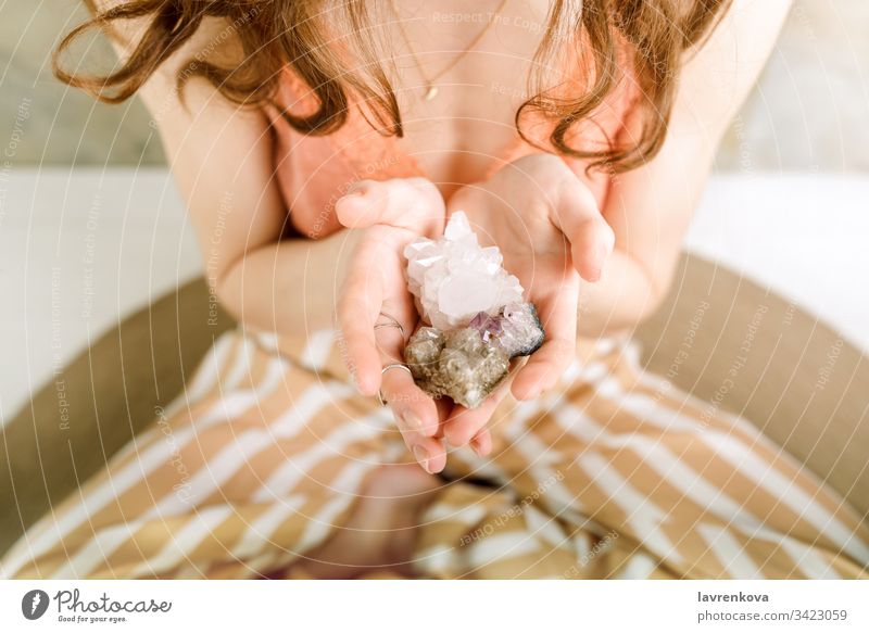 Closeup of woman's hands holding crystalls stones in her hands, shallow selective focus holistic magic rocks energy cozy home bra crystals faceless fashionable