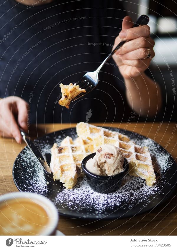 Anonymous person eating waffles with ice cream near coffee cafe cut sweet table sit fork knife delicious food tasty dessert fresh plate restaurant breakfast