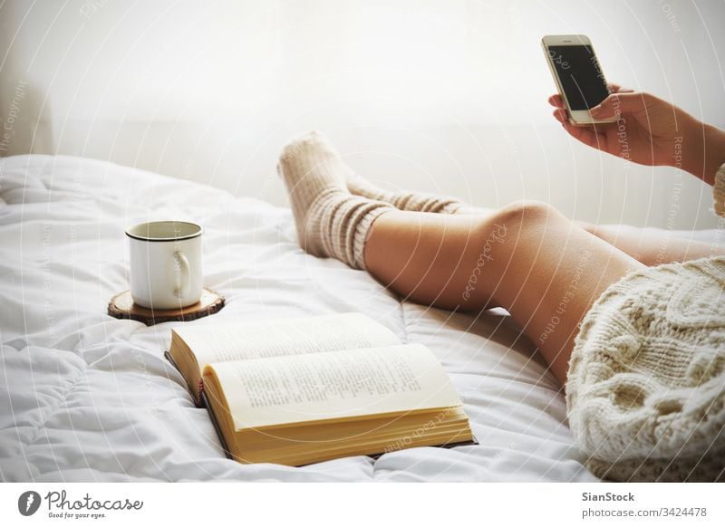 Soft photo of woman on the bed with old book, a cup of coffee and smart phone read reading window view lazy sunday winter tea morning girl home relax socks