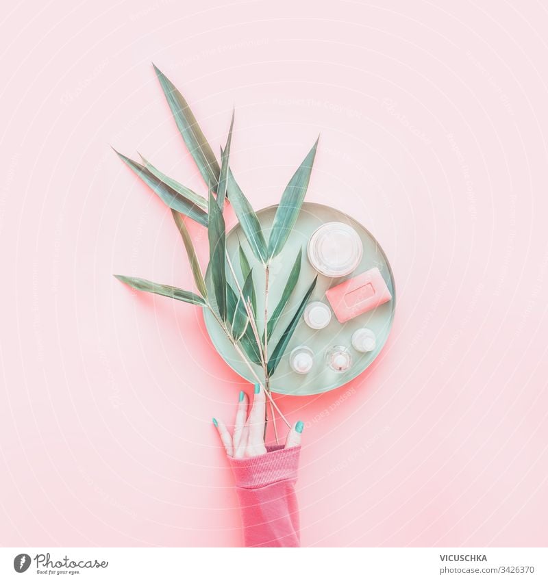 Female women hand with with bamboo branches and white cosmetic products on tray on pastel pink background. Top view. Beauty concept. Modern skin care. Flat lay. Layout. Natural cosmetic