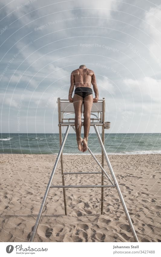 Gymnast at the stand from behind Man Beach Lifeguard Chrome Chair coached Strong exercise Waves Sand Horizon Clouds Swimming trunks muscle Acrobatics