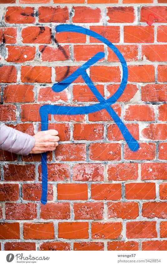 A woman's hand apparently holds a hammer and a sickle - graffito in front of a red brick wall Graffiti Graffito Hand Women`s hand hammer and sickle Brick wall