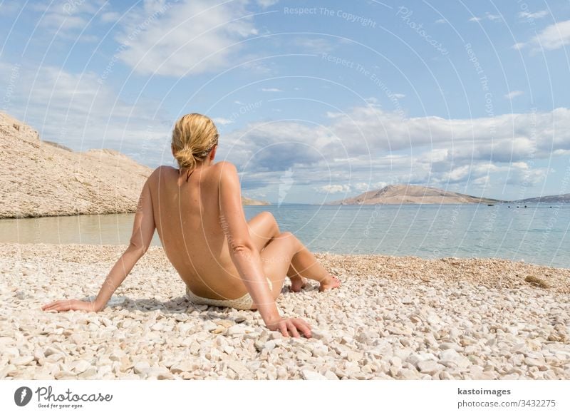 Rear view of sexy young caucasian woman sunbathing topless on romote pabble beach on Pag island, Croatia, Mediterranean. summer body tanning vacations beauty