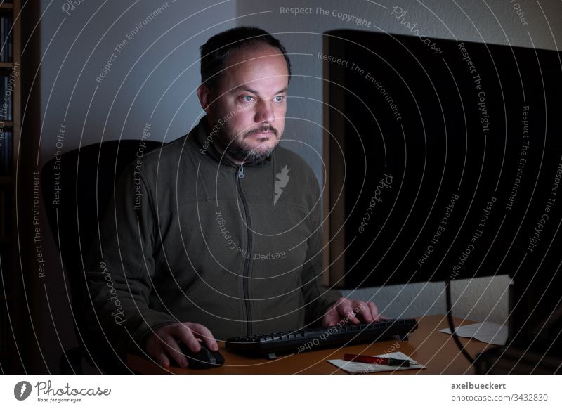 man sitting in front of computer at night pc screen desk home room technology internet work office online monitor using desktop addiction lifestyle mid age