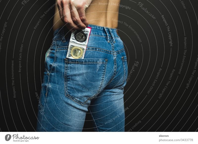young guy in jeans is preparing for a romantic date-puts a colored condom in the back pocket of his jeans. Body part: male ass. Concept: protection against sexually transmitted diseases