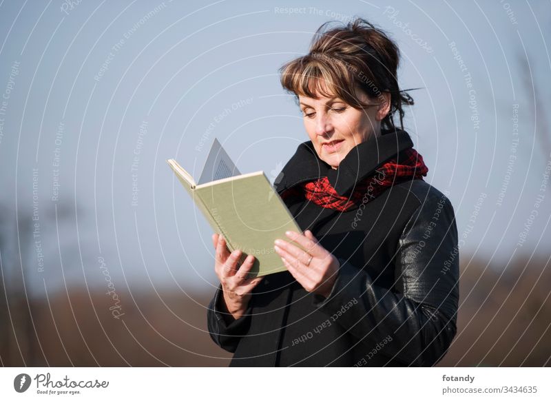 woman reading upper part 50s mittleres Alter Entspannung Frau Lederjacke Park allein Buch draußen eine erwachsen zufrieden Ablenkung Freizeit modisch Jacke