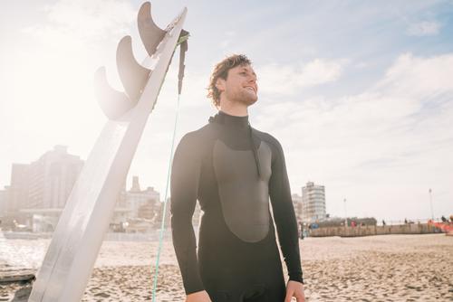 Surfer standing at the beach next to his surfboard. man water sport surfing sea surfer ocean outdoors athletic coastline waves background adventure sports