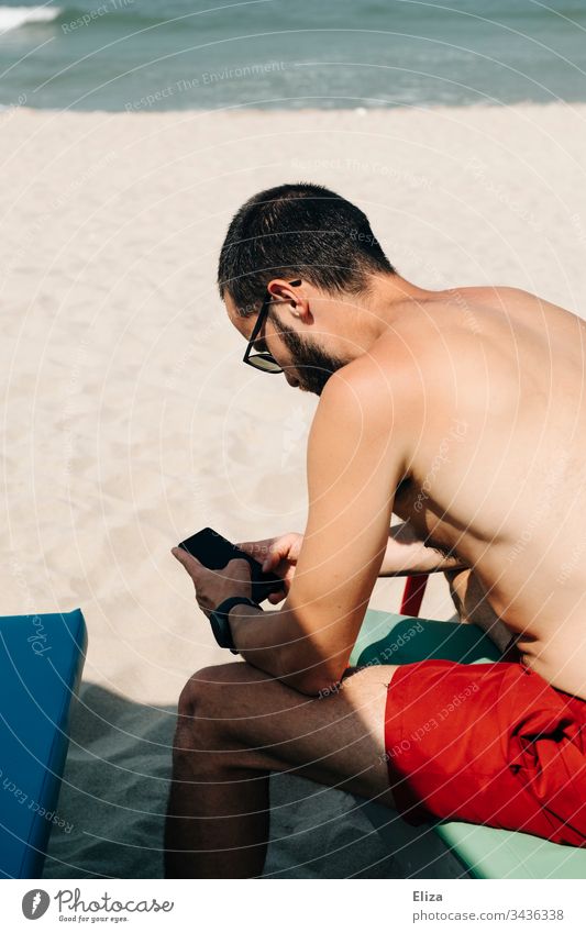 Stranded vacationer sits on the beach and is busy with his smartphone Holidaymakers corona covid-19 Beach travel Tourist stressed anxious Stress