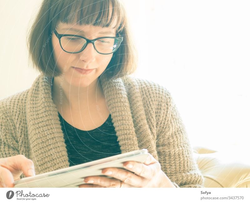 Caucasian woman with glasses using tablet work from home gadget device sitting caucasian portrait concentrated quarantine bob internet cozy closeup room