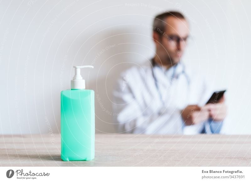 doctor man using mobile phone. Front focus on an alcohol gel or antibacterial disinfectant. Hygiene and corona virus concept. Covid-19 professional hospital