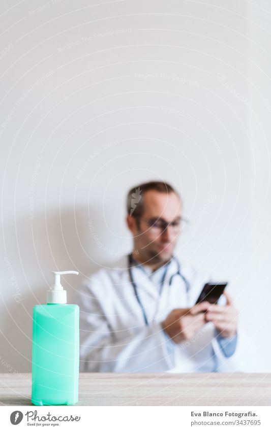 doctor man using mobile phone. Front focus on an alcohol gel or antibacterial disinfectant. Hygiene and corona virus concept. Covid-19 professional hospital