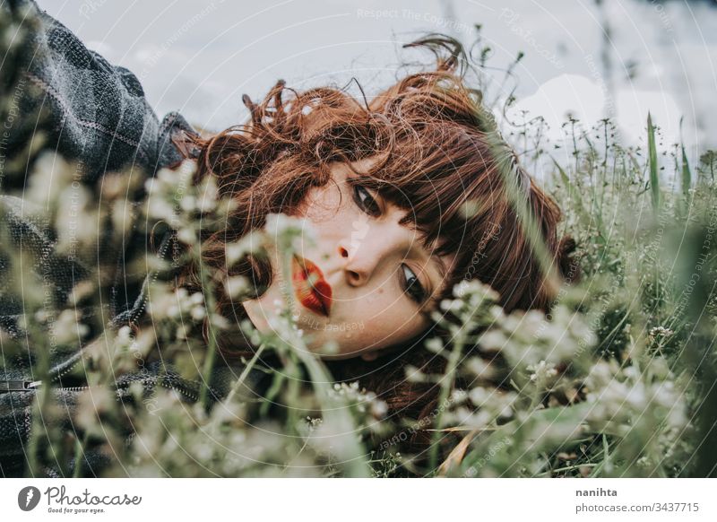 Young beautiful woman resting in a field of flowers portrait mood spring dark romantic nostalgia emotions green brunette pretty face white caucasian nature
