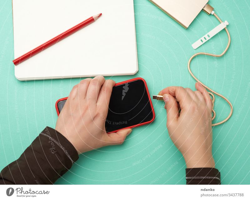 two hands holding a red mobile smartphone and a charging cable on a green background adapter adult caucasian cellphone charge charger communication connection