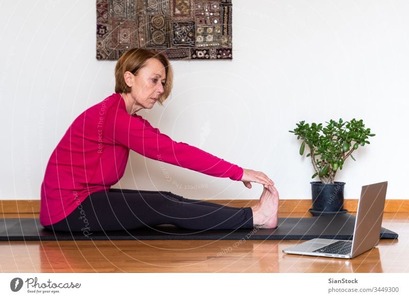 Middle aged woman watching yoga exercises online video tutorial  on her laptop. Yoga at home concept. bending beauty workout european exercising flexibility