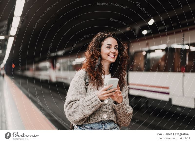 young beautiful woman at train station using mobile phone before catching a train. Back view. Travel, technology and lifestyle concept travel moving caucasian