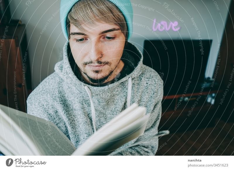 Young man reading a book in his home attractive quarantine hobby leisure relax enjoying learn study student young youth indoors room decoration life casual real