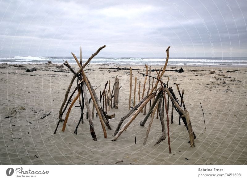Wooden tent on a beach in Oregon wooden Tent Beach Sand Ocean Water Gray inclement weather travel Beautiful vacation Rough Waves Sticks homemade