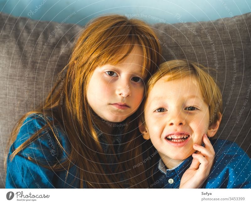 Two blonde little kids in blue shirts on sofa child smile face hug family love siblings brother sister redhead funny sweet tender together near indoors portrait