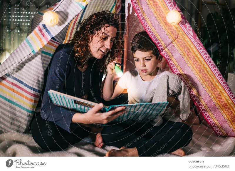 Mother and son reading a book on a tent at home beautiful bedroom bedtime caucasian child childhood concept cute dark daughter day education family female