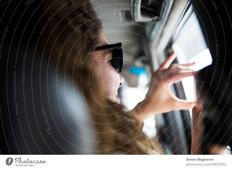 Cute young woman taking a photo with mobile phone from inside a vehicle on a road trip travel seat looking enjoying view day passenger sunglasses indoors