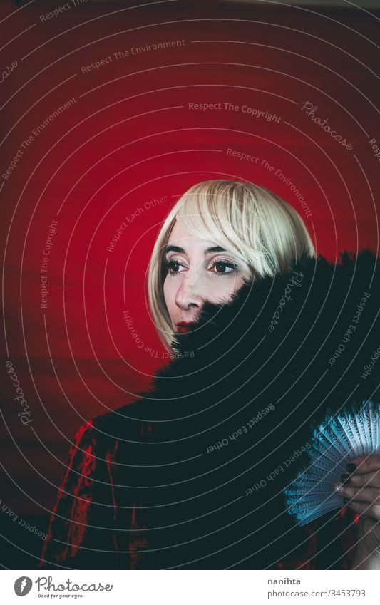 Vintage style portrait of a blonde woman covering by a hand fan mysteryous cabaret theatre custom actress vintage retro circus red black middle age dark