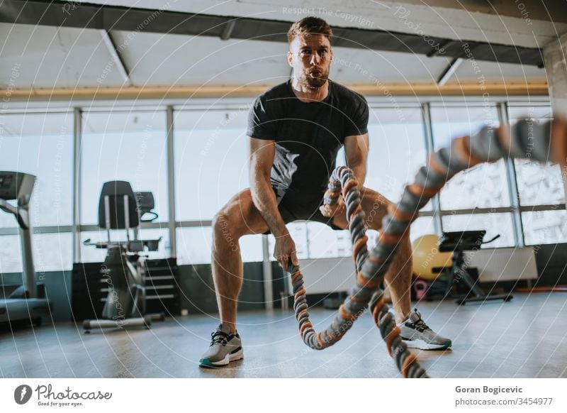 Young man practicing with battle ropes in the gym muscular strength fitness workout healthy sport male strong young exercise body muscle power athlete active