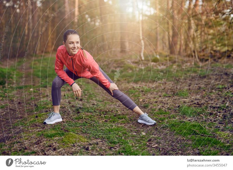 Full length portrait of a happy  fit young woman doing stretching exercises for legs and arms during outdoor workout in the forest in Springtime Happy confident