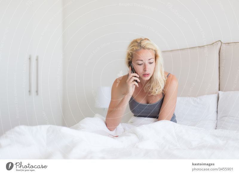 Woman talking by phone on bed in morning. woman call bedroom young person mobile white using pillows news home listening adult lonely interior wake motel