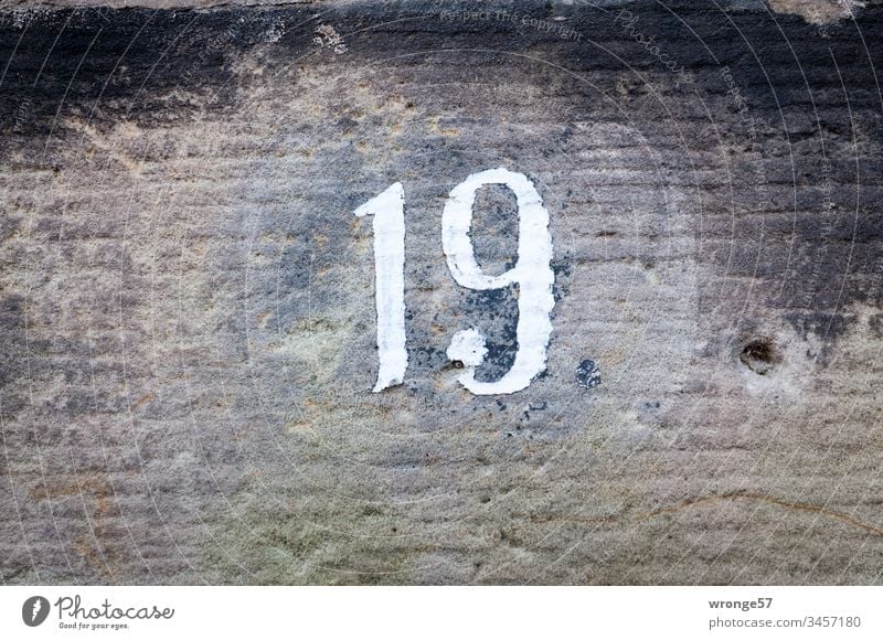 Figure 19 on a limestone wall Digits and numbers Close-up Exterior shot House number Orientation Colour photo Close-up view under natural lighting conditions